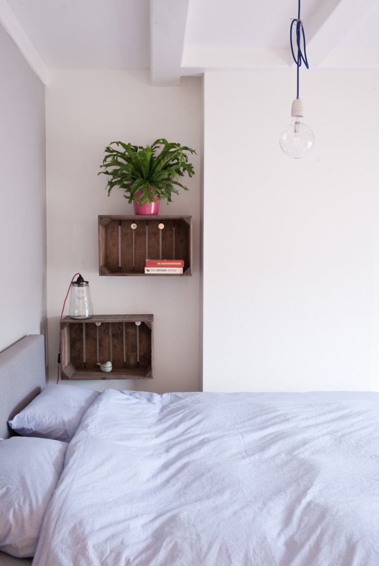 Naast het bed hangen houten kratjes, ideaal om boeken in op te bergen. De lamp is van I am Recycled.
